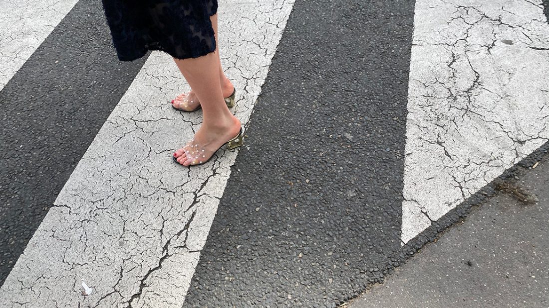 Une femme sexy avec des mules transparentes traverse la rue