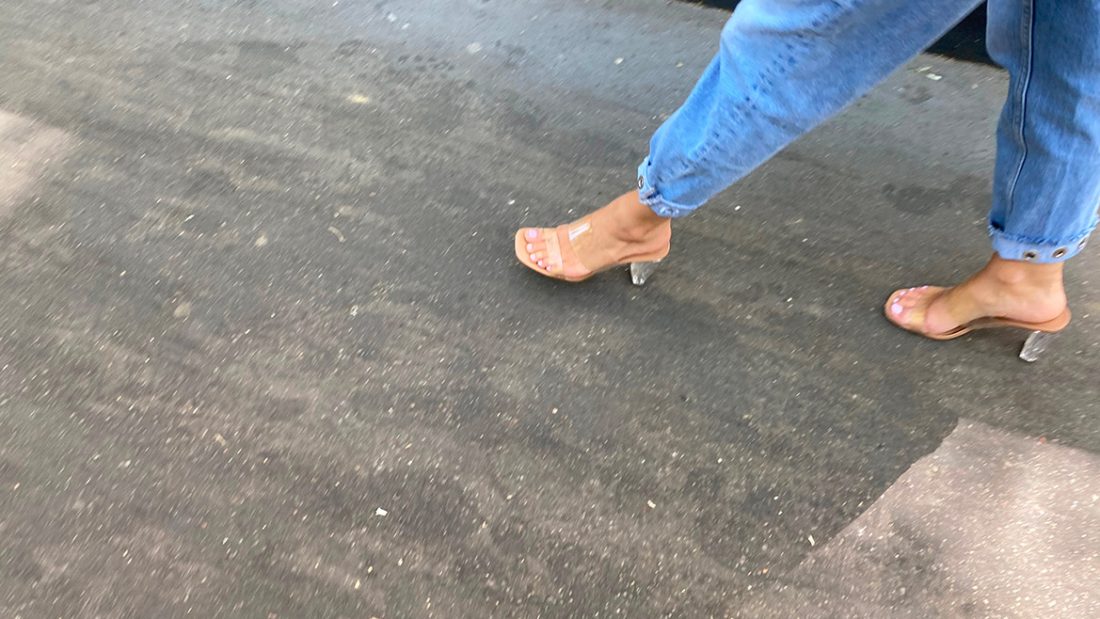 Une fille sexy avec des mules transparentes marche dans la rue
